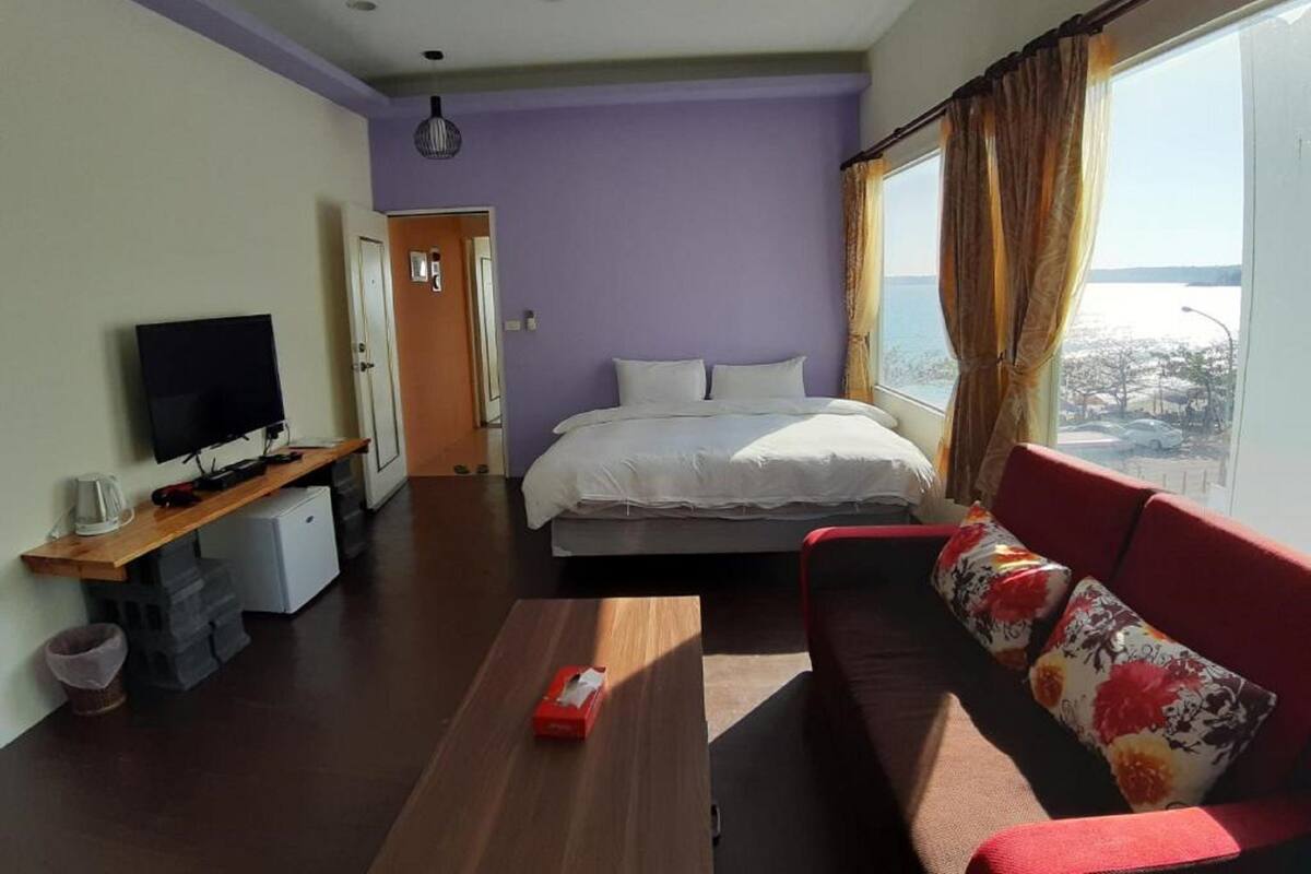 Habitació amb llit, televisió, sofà i finestra amb cortines.