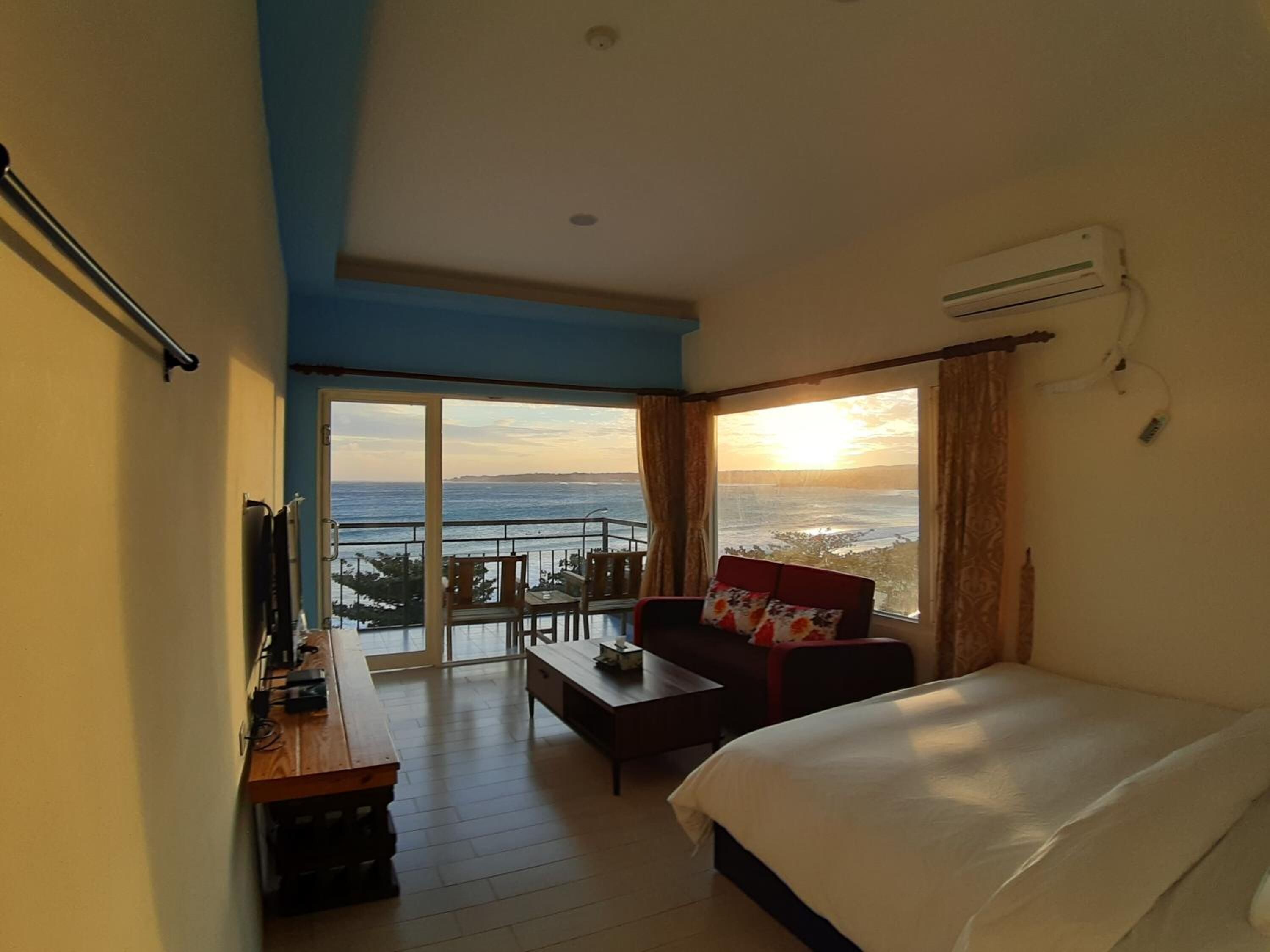Quarto de hotel com cama, escrivaninha, cadeira e varanda com vista para o mar.