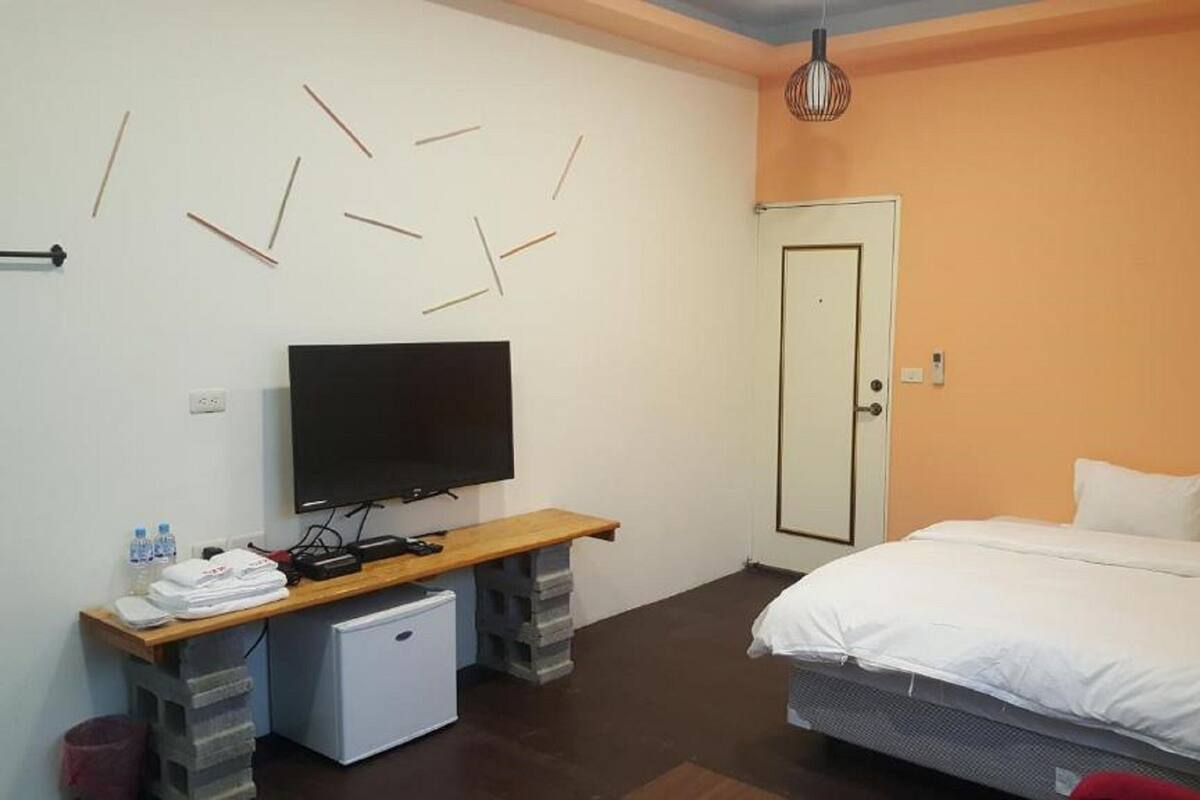 Un dormitori amb llit, televisió, nevera petita i escriptori amb cadira.