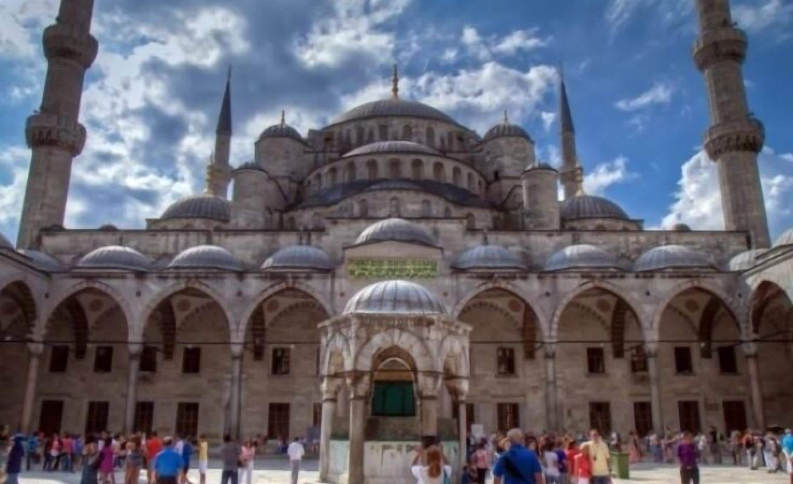 Un bâtiment historique doté de plusieurs dômes et de minarets, avec une cour intérieure ouverte où les visiteurs peuvent se promener.