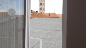 Une vue à travers la fenêtre d’un bâtiment doté d’une tour, d’un toit recouvert de tuiles et surplombant un ciel dégagé.