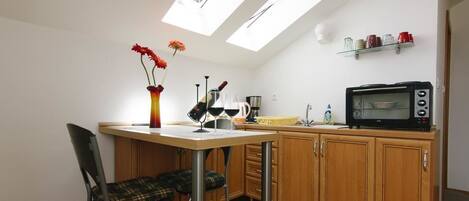 Una cocina compacta con comedor, microondas y una repisa con tazas.