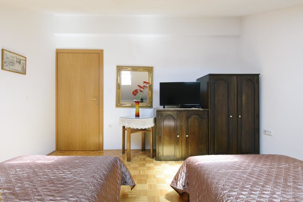 Une chambre avec deux lits, une armoire en bois, un téléviseur posé sur un meuble, une petite table avec un vase et une porte.