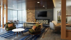 A modern living area with a stone wall, a flat-screen TV, and a blue patterned rug. - Fairfield Inn & Suites by Marriott Riverside Moreno Valley (Moreno Valley)