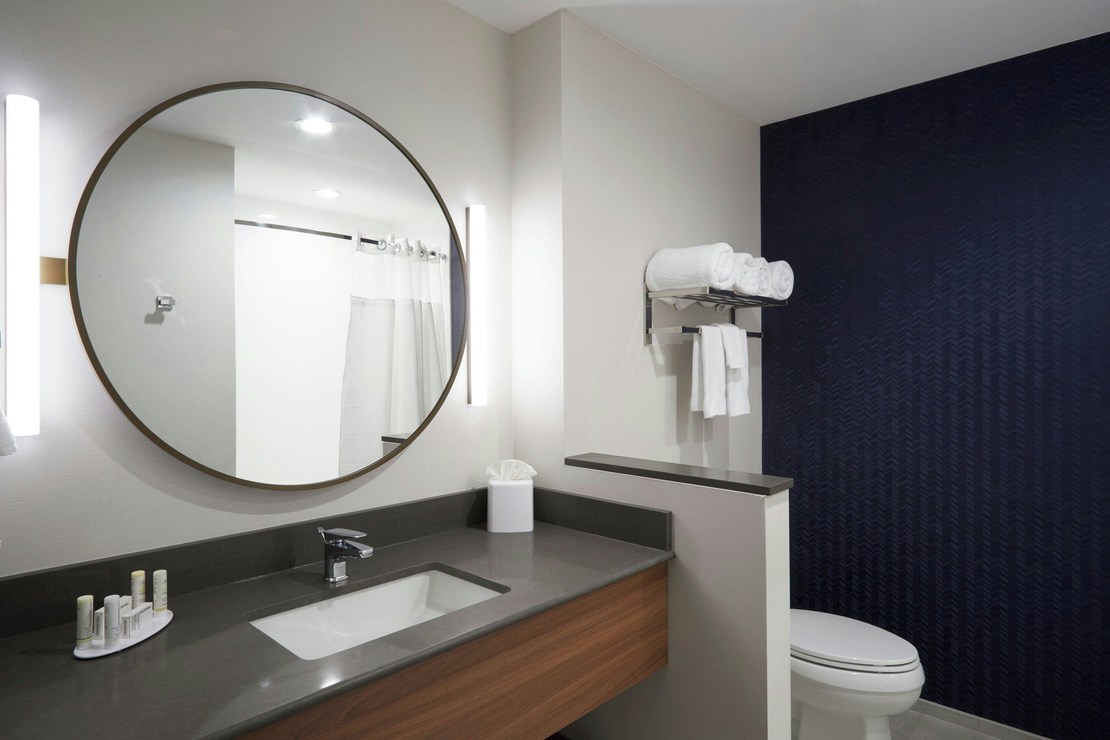 A modern bathroom with a round mirror, a sink, and a toilet.