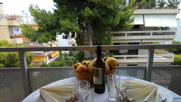 A table set for two with a bottle of wine, glasses, plates, and a basket of fruit. - Top Floor Cozy Apartment near Beach (Vari-Voula-Vouliagmeni)