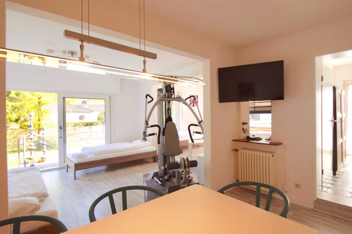 Een kamer met een bed, fitnessapparatuur, een televisie en een eethoek.