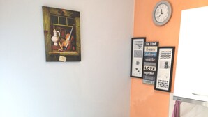 Een kleine keuken met een witte koelkast, een fornuis en een tafel met stoelen. Er hangt een klok aan de muur en er zijn verschillende ingelijste foto's.