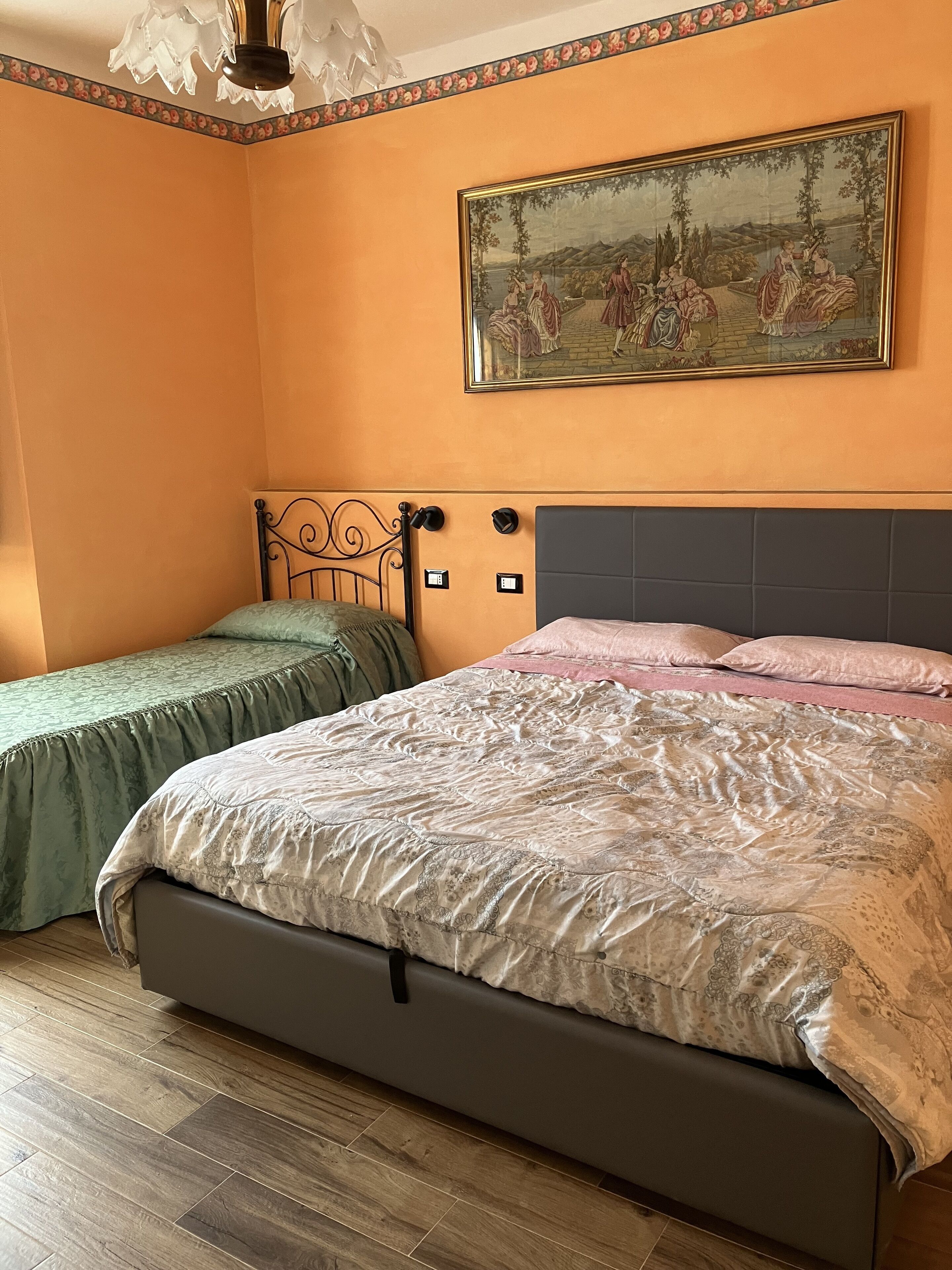 A bedroom with a large bed, two bedside tables, a nightstand, a painting on the wall, and a ceiling light fixture.