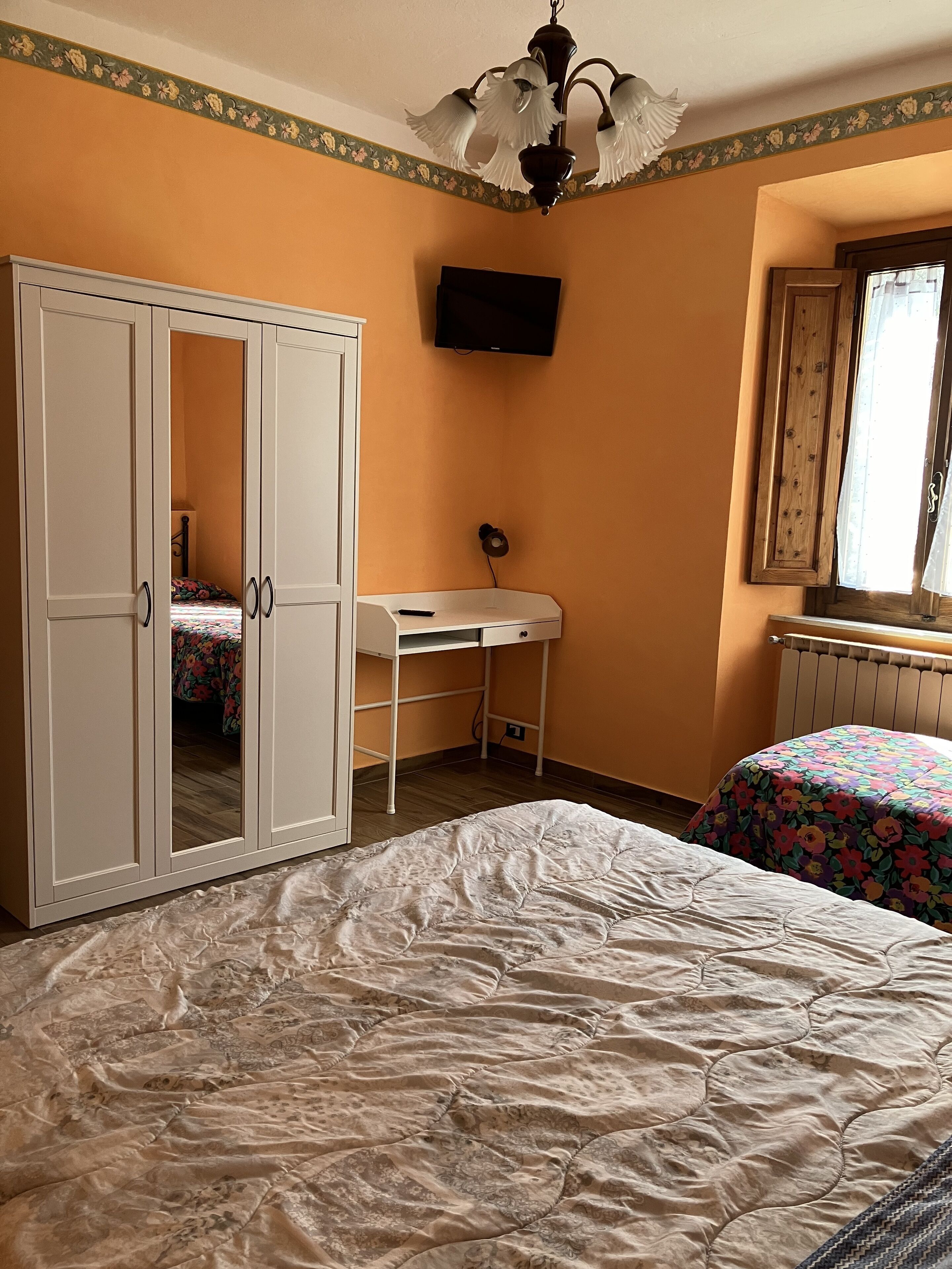 A bedroom with a bed, a desk, a wardrobe, and a television.