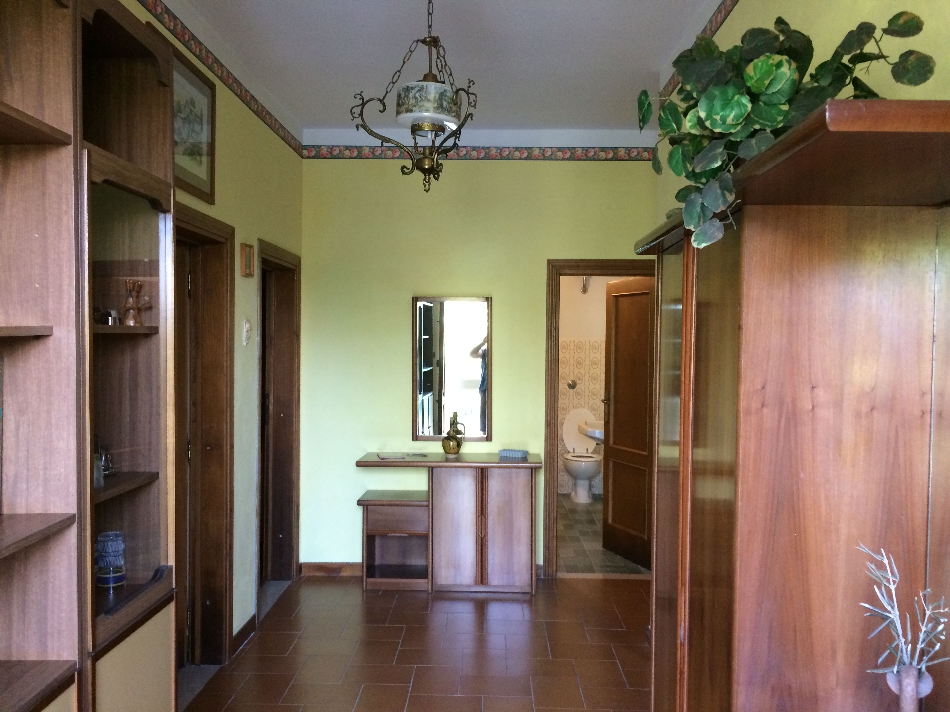 Un pasillo con estanterías de madera, un espejo y una puerta que da a un baño.