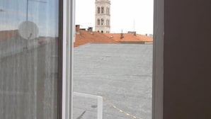 Blick durch ein Fenster auf ein Gebäude mit einem Turm, einem Ziegeldach und blauem Himmel.