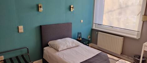 Una habitación con una cama, un banco, una mesa con lámpara y una ventana con persianas.