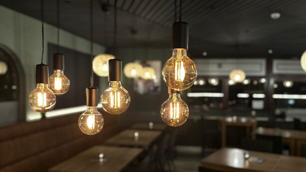 Een restaurantinterieur met hangende, bolvormige lampen, houten tafels en banken.