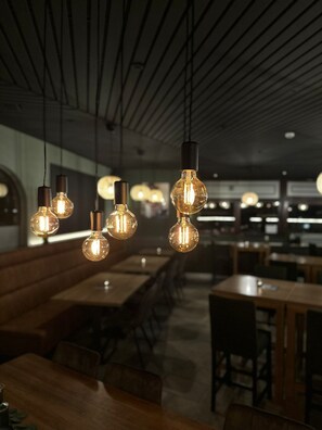 Een restaurantinterieur met hangende, bolvormige lampen, houten tafels en banken.