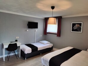 A bedroom with two beds, a desk, a chair, a TV, and a window with curtains.