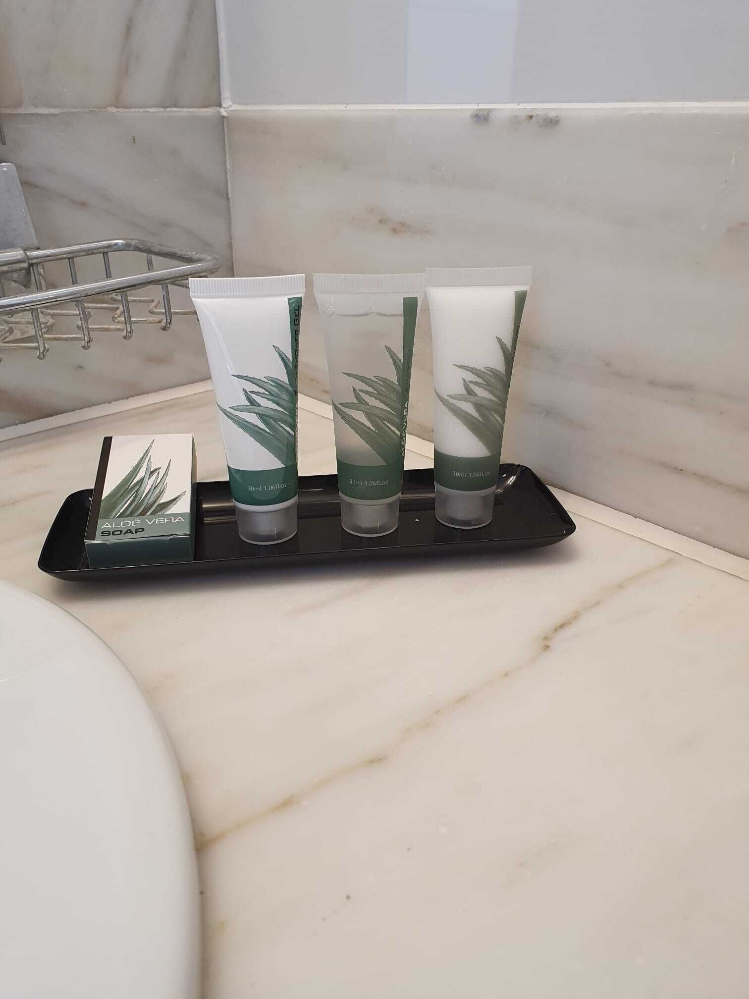 A bathroom with a marble countertop, a black soap dispenser, and three aloe vera soap tubes.