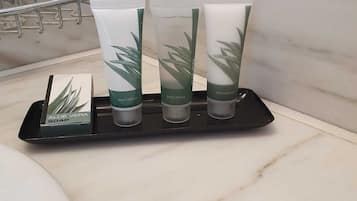 A bathroom with a marble countertop, a black soap dispenser, and three aloe vera soap tubes.