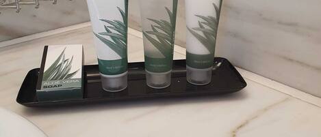 Un baño con encimera de mármol, dosificador de jabón negro y tres tubos de jabón de aloe vera.