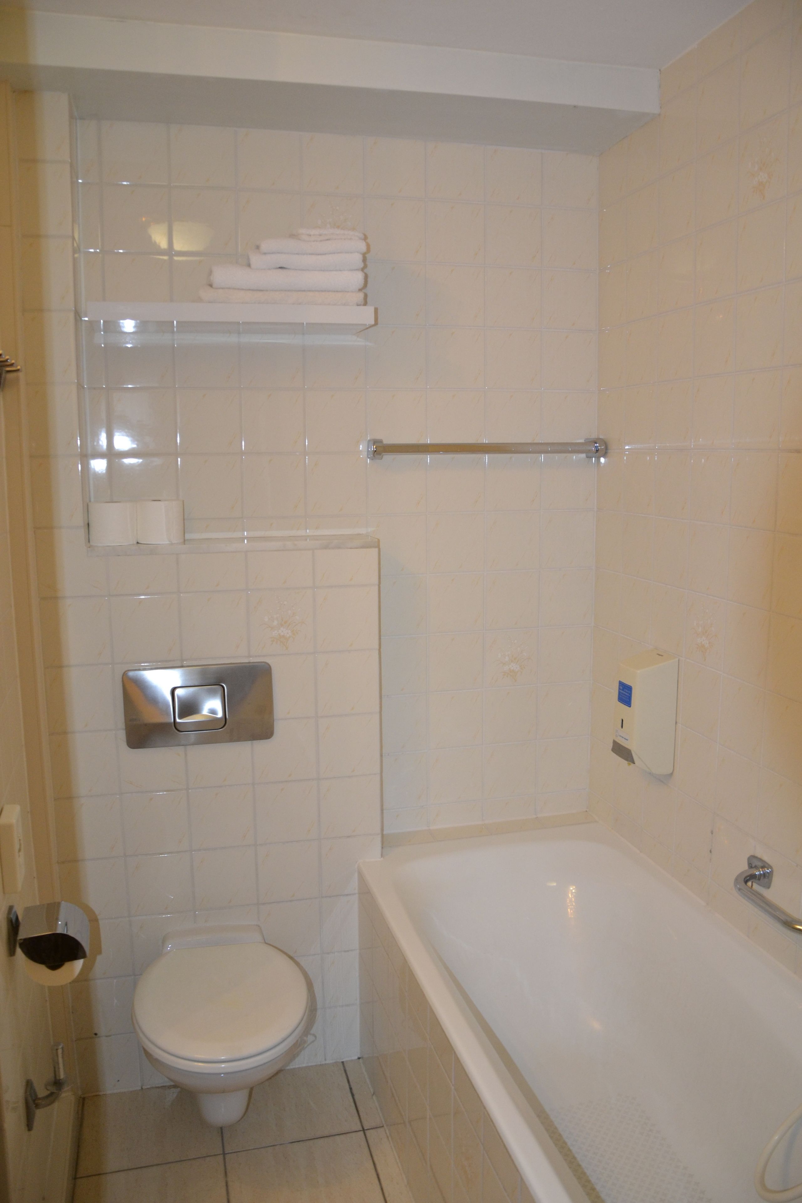 Un baño con inodoro, bañera, toallero y dispensador de jabón.