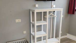 Een kamer met een witte inbouwkast, een aan de muur bevestigde televisie en een klein vloerluik.