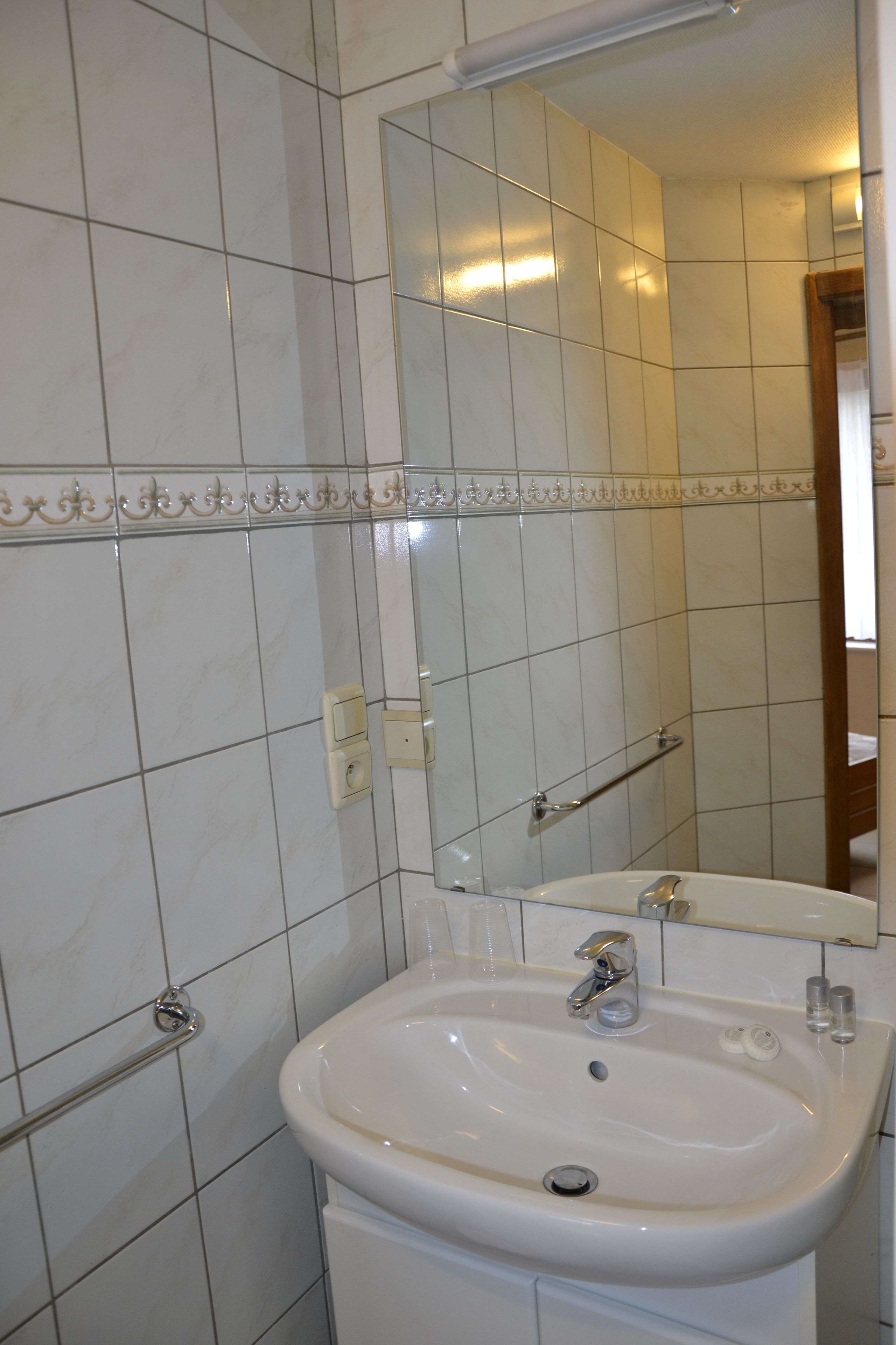 A bathroom with white tiled walls, a white sink with a mirror above it, and a towel rack.