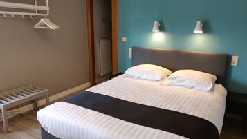 A neatly made bed with a grey headboard, two bedside lamps, and a wooden bench with a hanging rack.