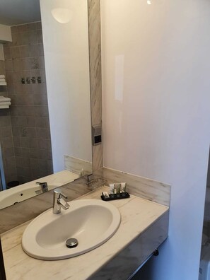 A modern bathroom with a marble sink, a large mirror, and a towel rack.