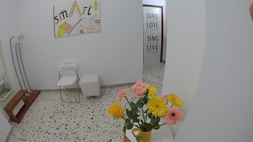 Una stanza con una sedia bianca, un tavolino, un vaso con fiori e manifesti motivazionali alle pareti.