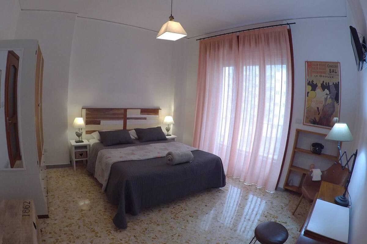 A bedroom with a bed, bedside tables, a lamp, a poster on the wall, and a door.