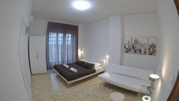 Una camera d'albergo moderna con un letto, una poltrona, un tavolino in vetro e un punto luce a parete.
