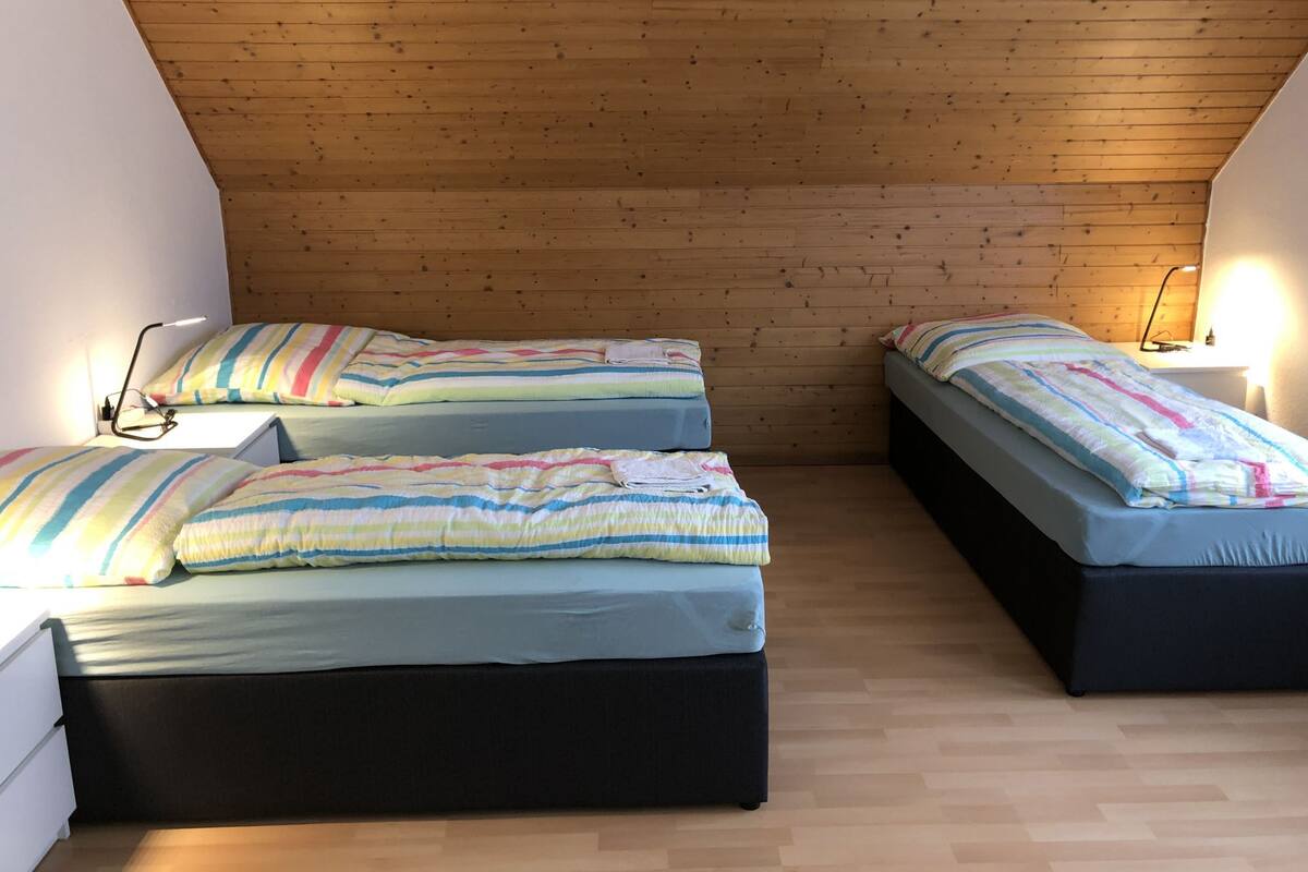 Quarto com duas camas, teto de madeira e luminárias de cabeceira.