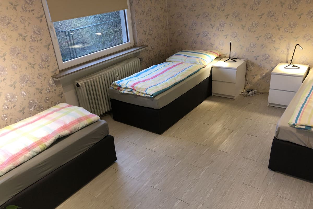 Quarto com duas camas, um radiador, uma janela e uma mesa de cabeceira com abajur.
