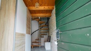Un escalier en colimaçon avec une finition en bois, menant à un palier doté d’un mur blanc et d’un mur extérieur vert.