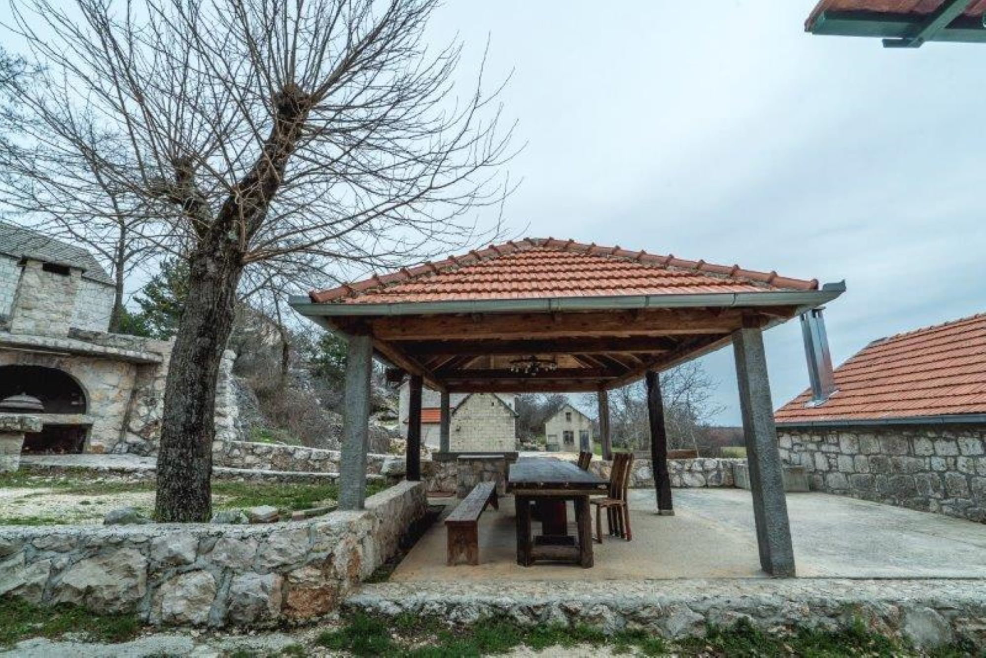 Ένα κτίριο από πέτρα με μια σκεπαστή, υπαίθρια περιοχή για καθιστικό, η οποία περιλαμβάνει ένα τραπέζι και παγκάκια.
