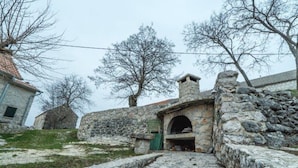 Un bâtiment en pierre doté d’un petit portail en arc, entouré d’arbres sans feuilles et d’un mur de pierre.