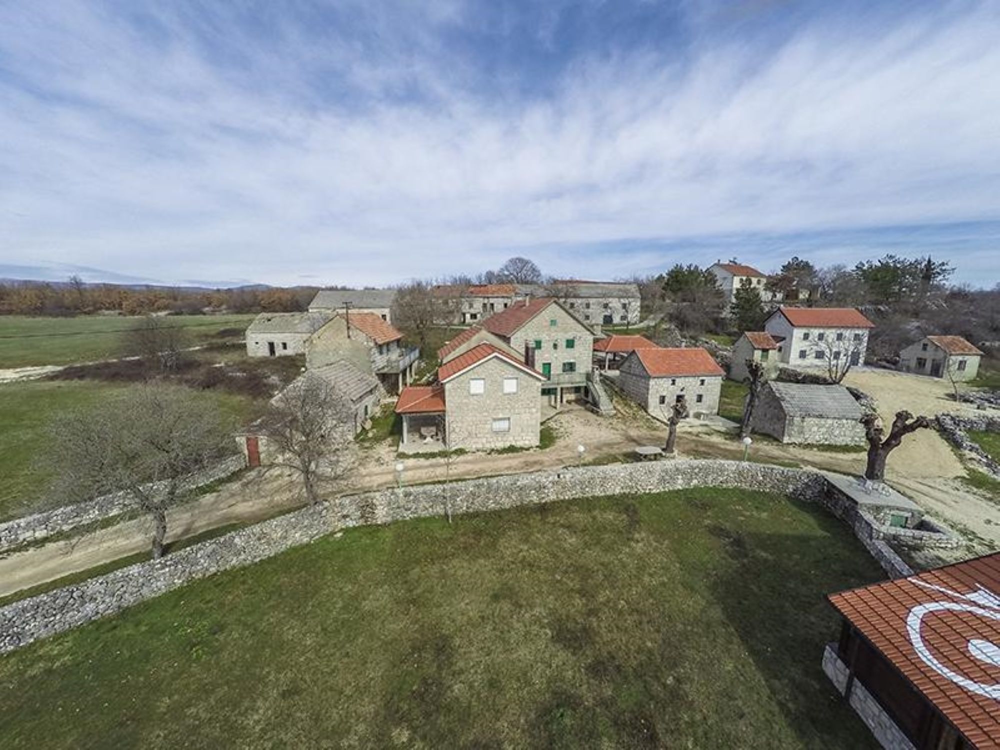 A cluster of stone buildings with red roofs, surrounded by open fields and a stone wall.