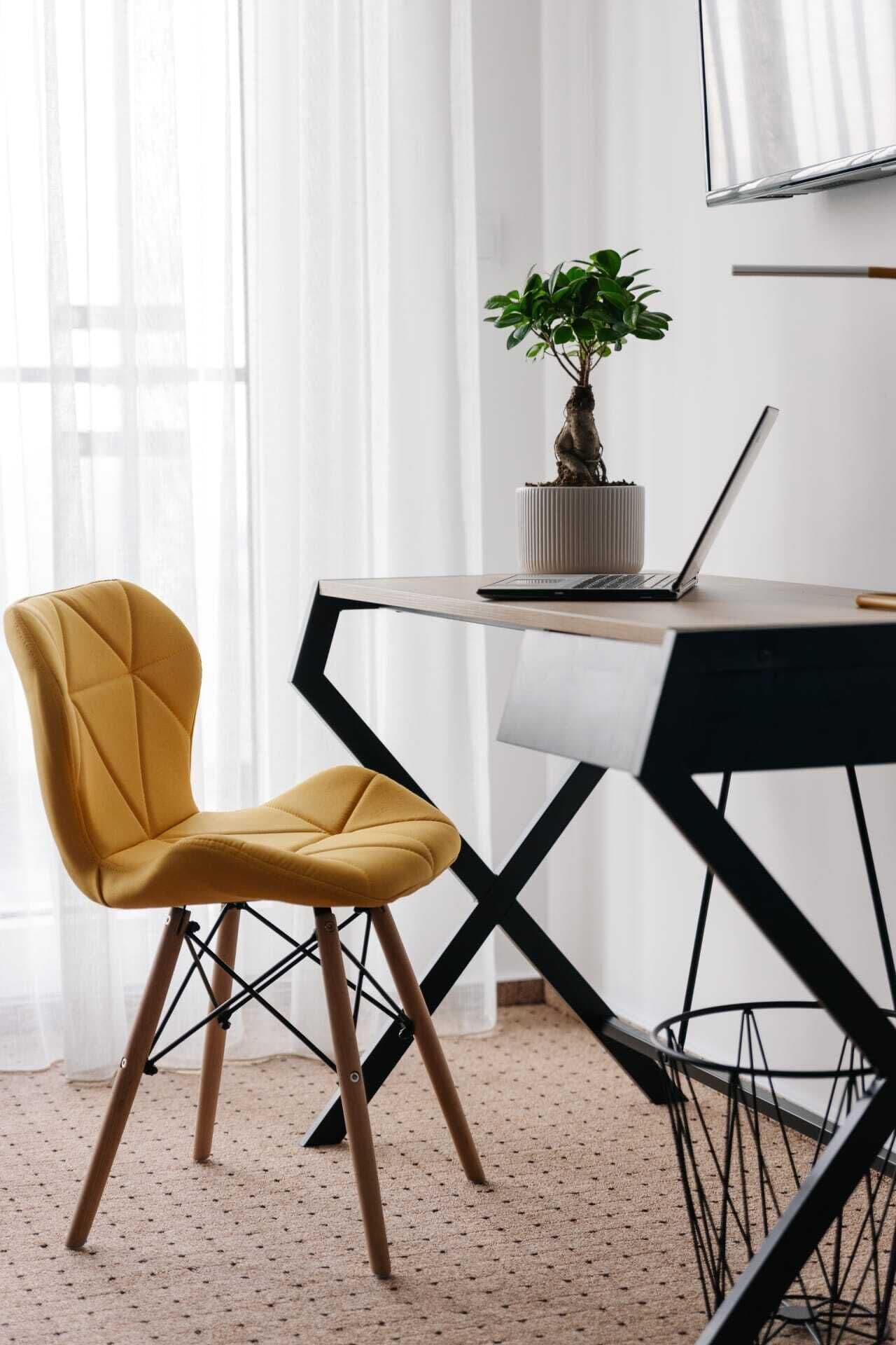 A modern office space with a yellow chair, a laptop on a desk, and a potted plant.