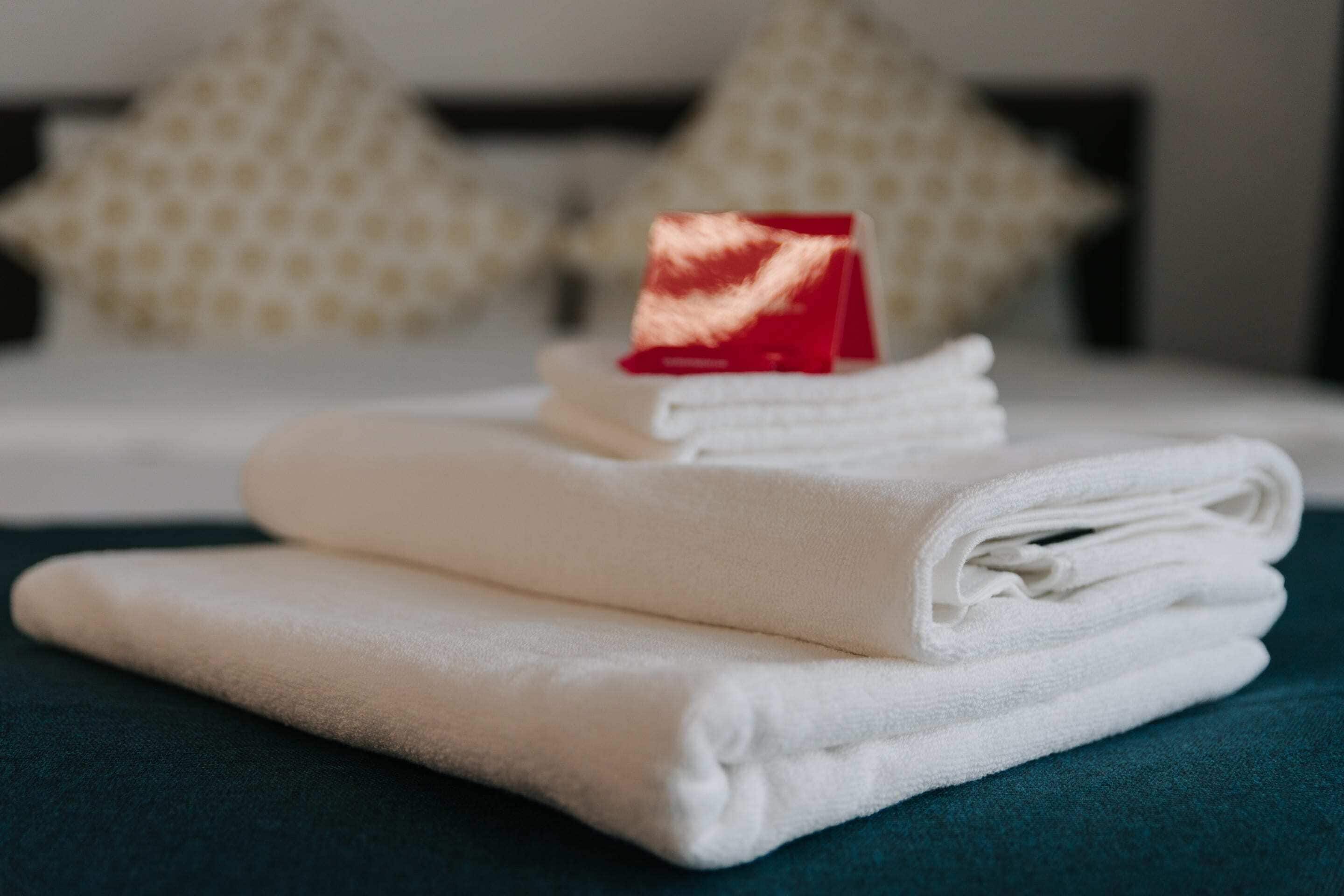 A neatly folded stack of white towels on a teal surface, with a red object on top.