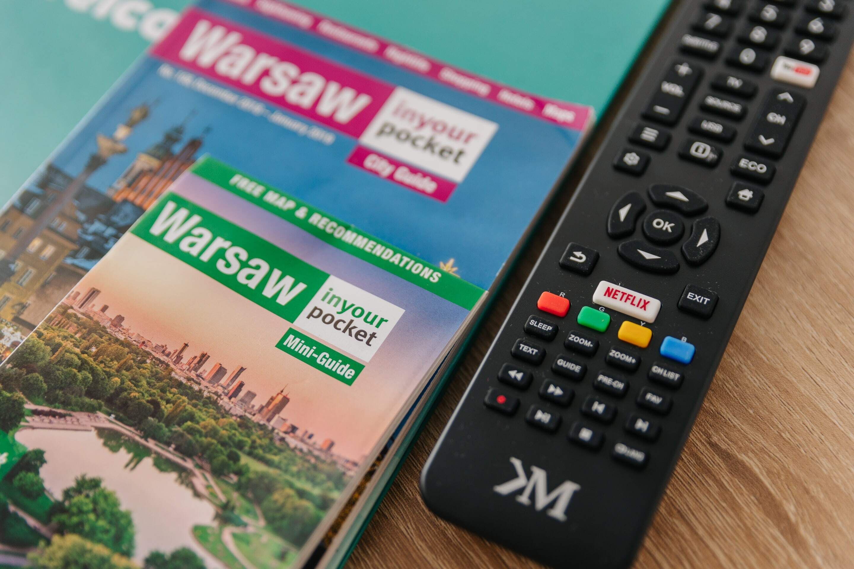 A travel guidebook titled 'Warsaw in Your Pocket' and a remote control with a Netflix button.