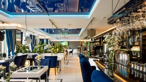 A modern restaurant with a long counter, blue upholstered seating, and a bar area with hanging glasses. - Varsovia Comfort Studios (Warsaw)