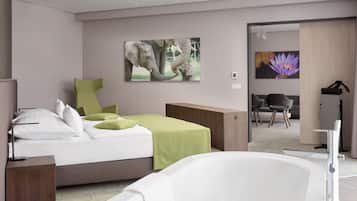 A modern bedroom with a bed, a green chair, a wooden side table, and a bathtub.