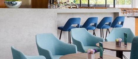 A modern interior with teal chairs, round tables, and a bar area with a plant.