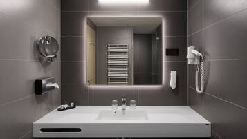 A modern bathroom with a white sink, a towel dispenser, a mirror, and a hairdryer.