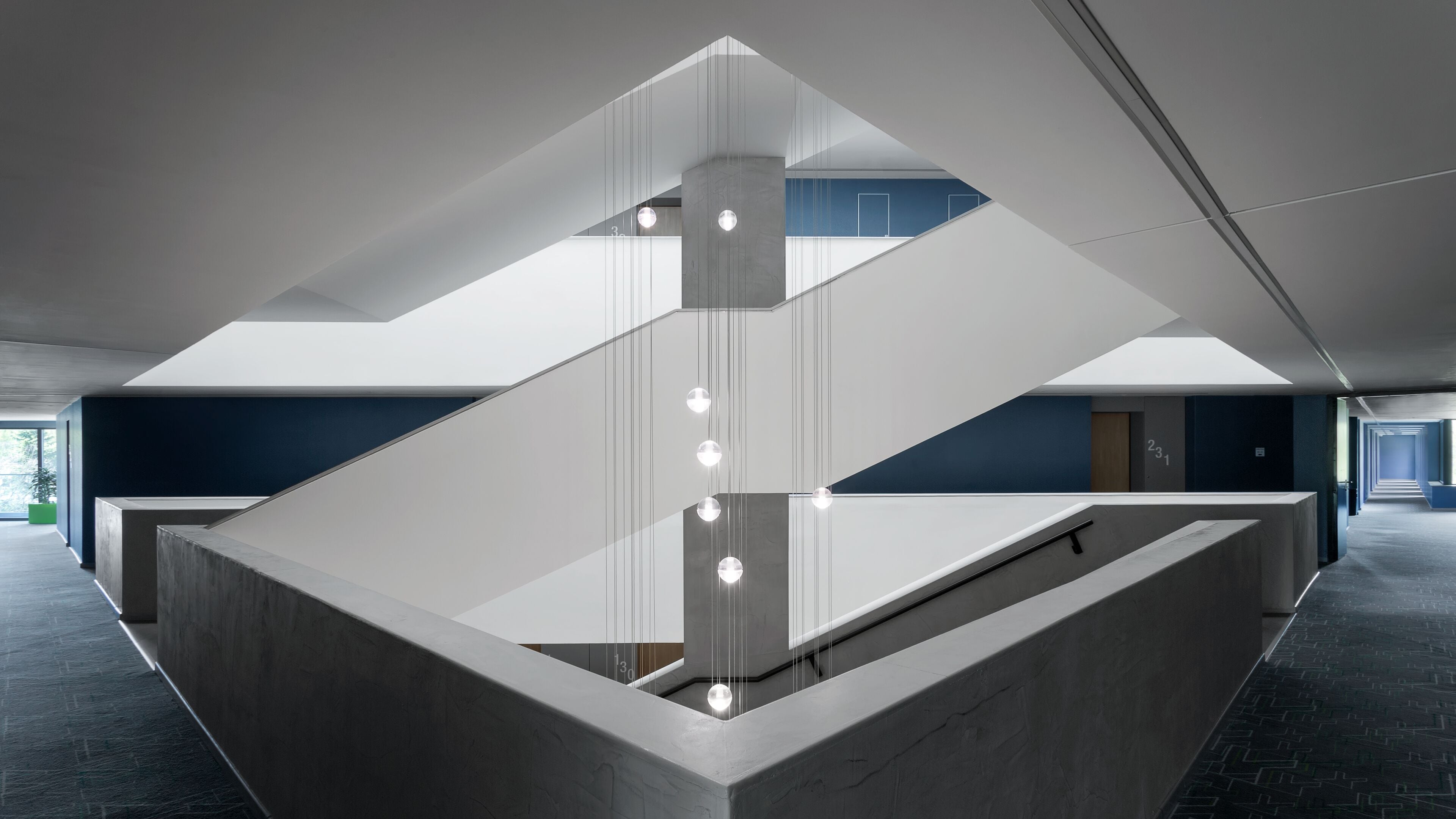 A modern interior with a geometric staircase design, a central light fixture, and a view of a hallway.