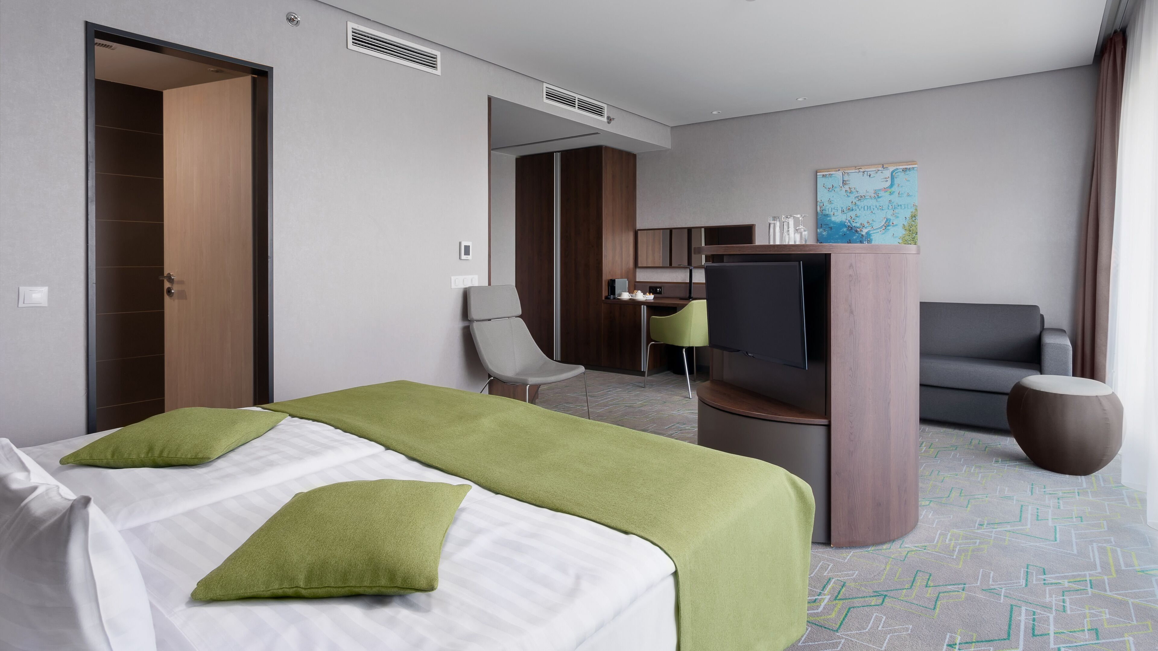 A hotel room with a bed, a desk, a chair, a television, and a map on the wall.