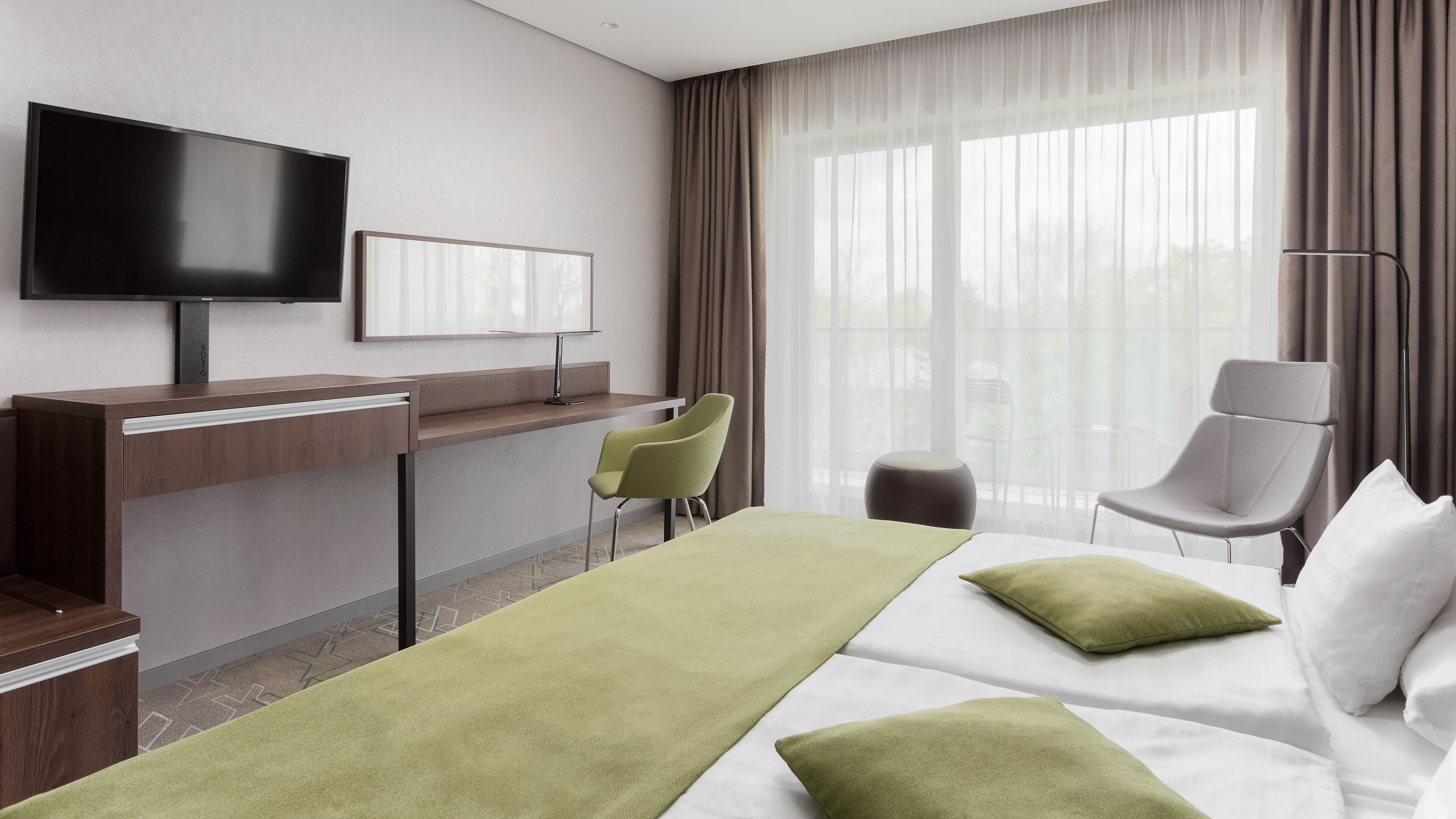 A hotel room with a bed, a desk, a chair, a TV, and a window with curtains.