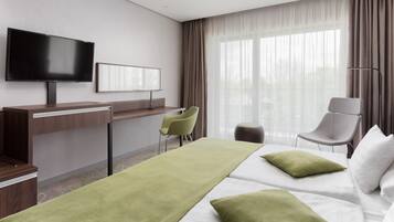 A hotel room with a bed, a desk, a chair, a TV, and a window with curtains.