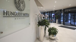 A modern hotel lobby with a large sign for HUNGUEST HOTELS HUNGARY, large potted plants, and a glass entrance. - Hunguest Hotel Sóstó (Nyiregyhaza)