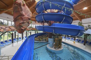 Un tobogán de agua interior con varios niveles y una zona de piscina con sillones de descanso.